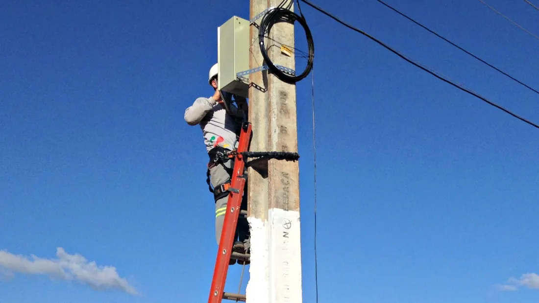 Técnico da Tchêturbo em uma escada instalando uma caixa de fibra óptica no alto de um poste, em 2014