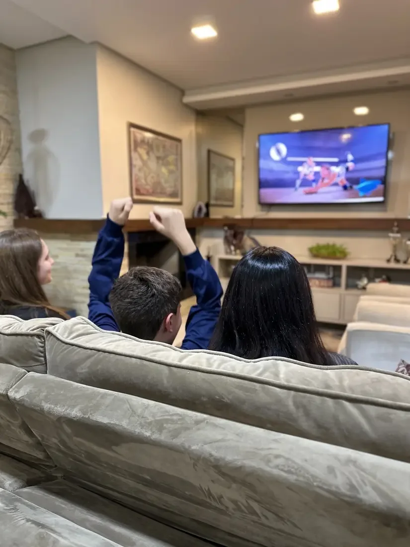 Três crianças comemorando no sofá diante da televisão, assistindo à Turbo TV em casa, em 2023